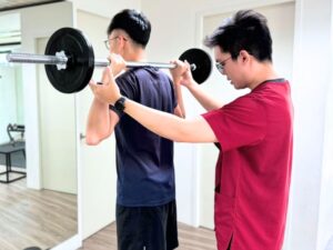 Physiotherapist supervising a patient's overhead barbell press during post-surgery rehabilitation