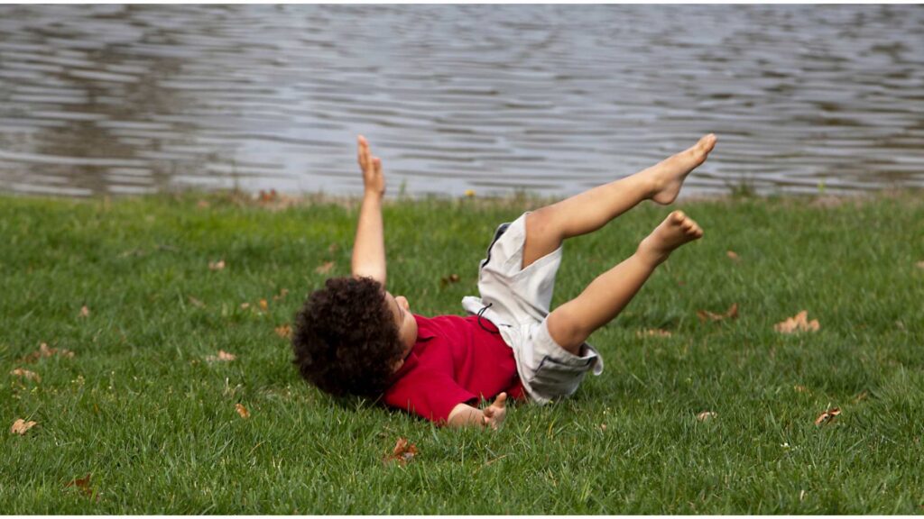 A young child falls on the grass near a lake, highlighting the importance of balance, coordination, and motor skills. Paediatric physiotherapy helps children improve movement control and prevent falls through targeted exercises.