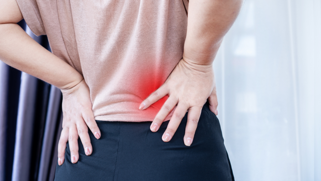 A person holding their lower back in discomfort, indicating pain and tension. Physiotherapy and posture correction can help alleviate chronic lower back pain and improve mobility.