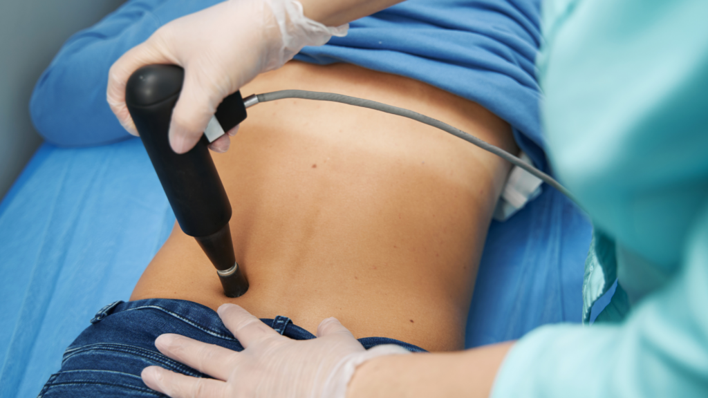 A physiotherapist performing shockwave therapy on a patient's lower back to relieve pain and promote healing.