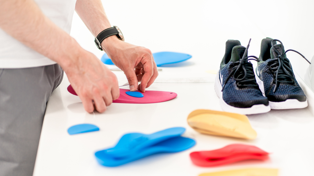 A podiatrist customising insoles with precision adjustments, surrounded by various orthotic inserts and a pair of running shoes, highlighting the importance of personalised foot support.