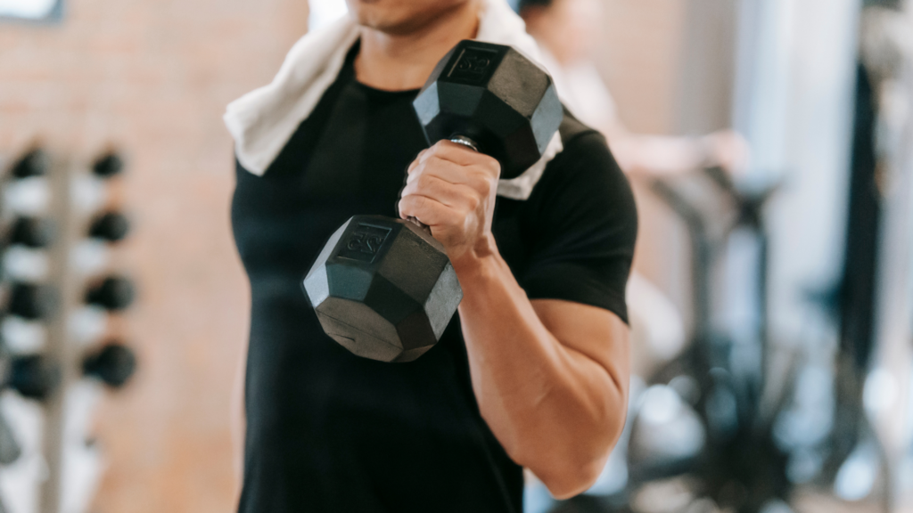  A man lifting a heavy dumbbell in a gym, focusing on strength training. Proper technique and physiotherapy can help prevent sports injuries and enhance performance.