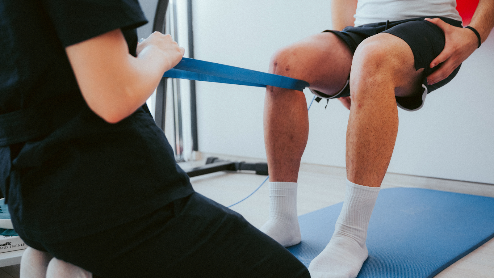 Physiotherapist treating patient with resistance band for knee rehabilitation related to stress fracture.