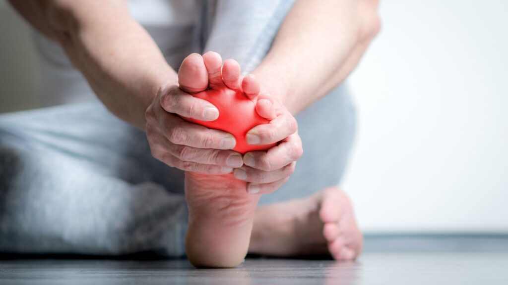 Person holding their foot with visible redness at the sole, representing plantar fasciitis and heel pain.