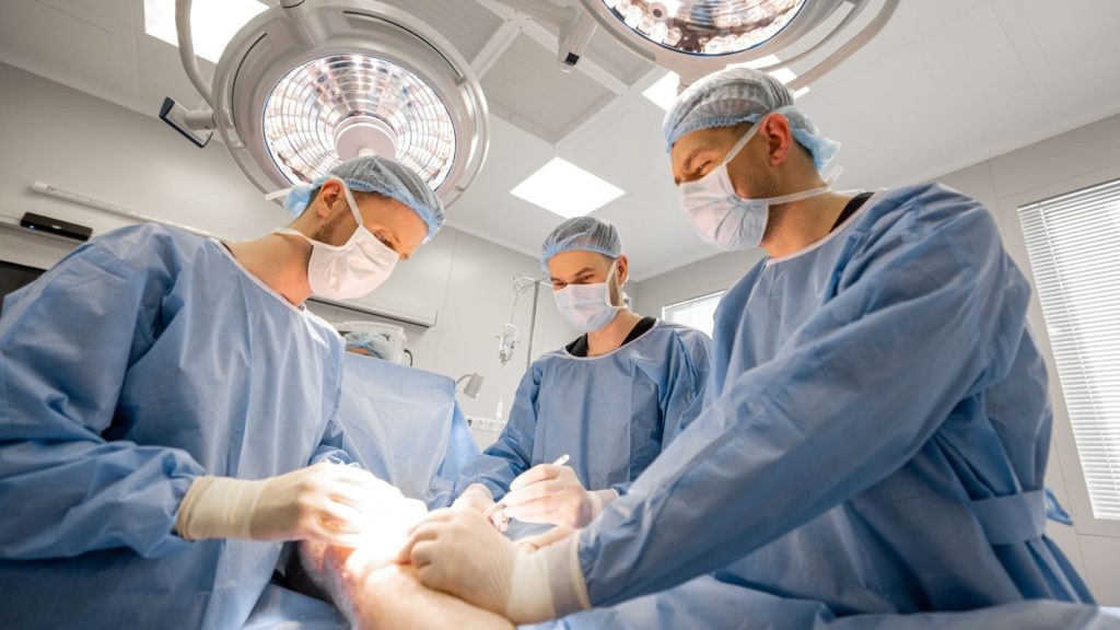 Orthopaedic surgeons performing knee surgery in an operating theatre.
