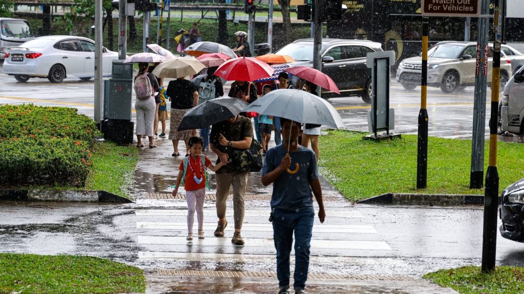 Pedestrians walking under umbrellas during a rainy, humid day in Singapore, illustrating year-round moisture and tropical climate conditions.