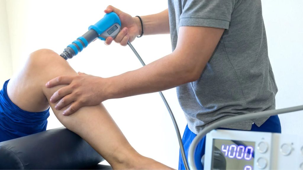 Physiotherapist applying shockwave therapy to the knee as part of a gradual tendon recovery programme