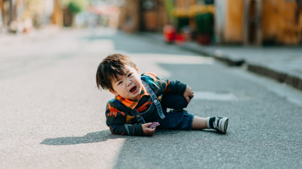 Toddler seated on the road after stumbling, representing early balance and coordination development in young children.