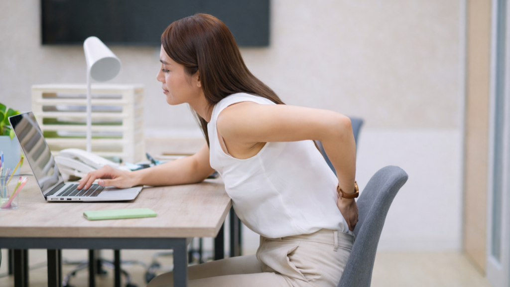 Asian office worker leaning forward with poor posture while using a laptop, illustrating forward head posture linked to jaw pain.