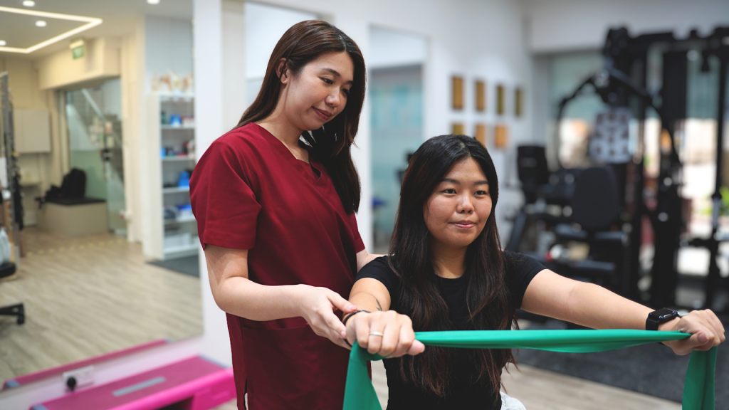 Physiotherapist guiding an adult through shoulder and arm strengthening using a resistance band in a rehabilitation clinic