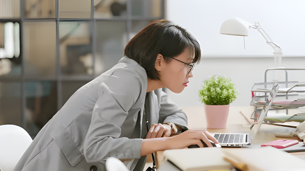 Office worker leaning forward while using laptop illustrating tech neck posture that can cause tension headaches