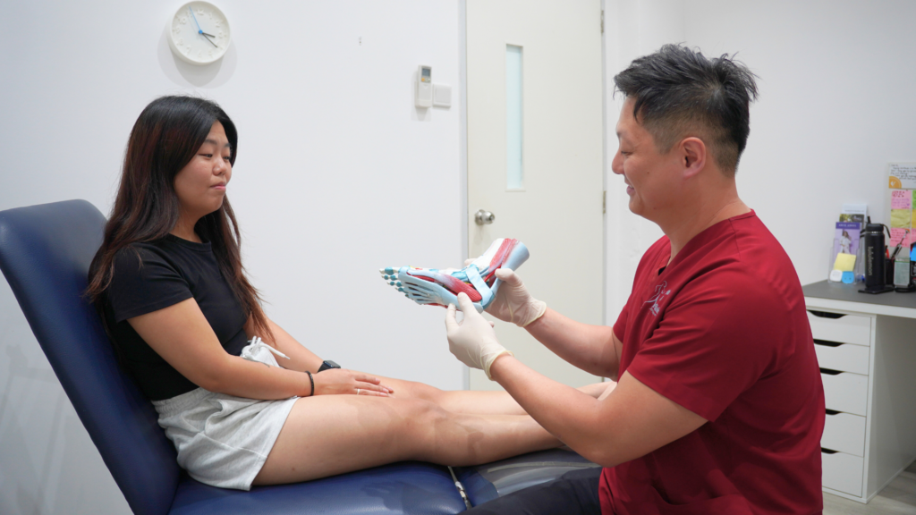Podiatrist explaining foot anatomy and footwear support to a patient during a clinic consultation. 