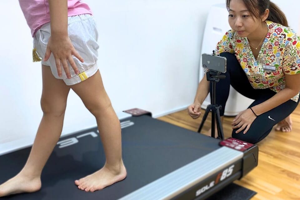 Child walking on a treadmill while a podiatrist films their gait for assessment
