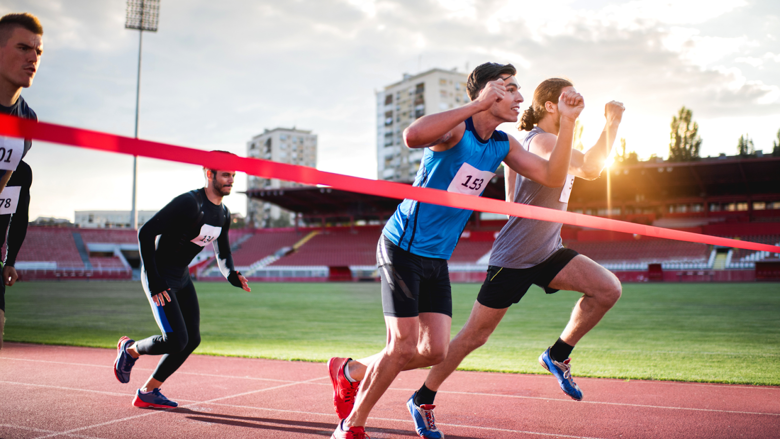 Athletes sprinting to the finish line in a stadium setting, symbolising the performance goals that sports physiotherapy can help clients achieve.
