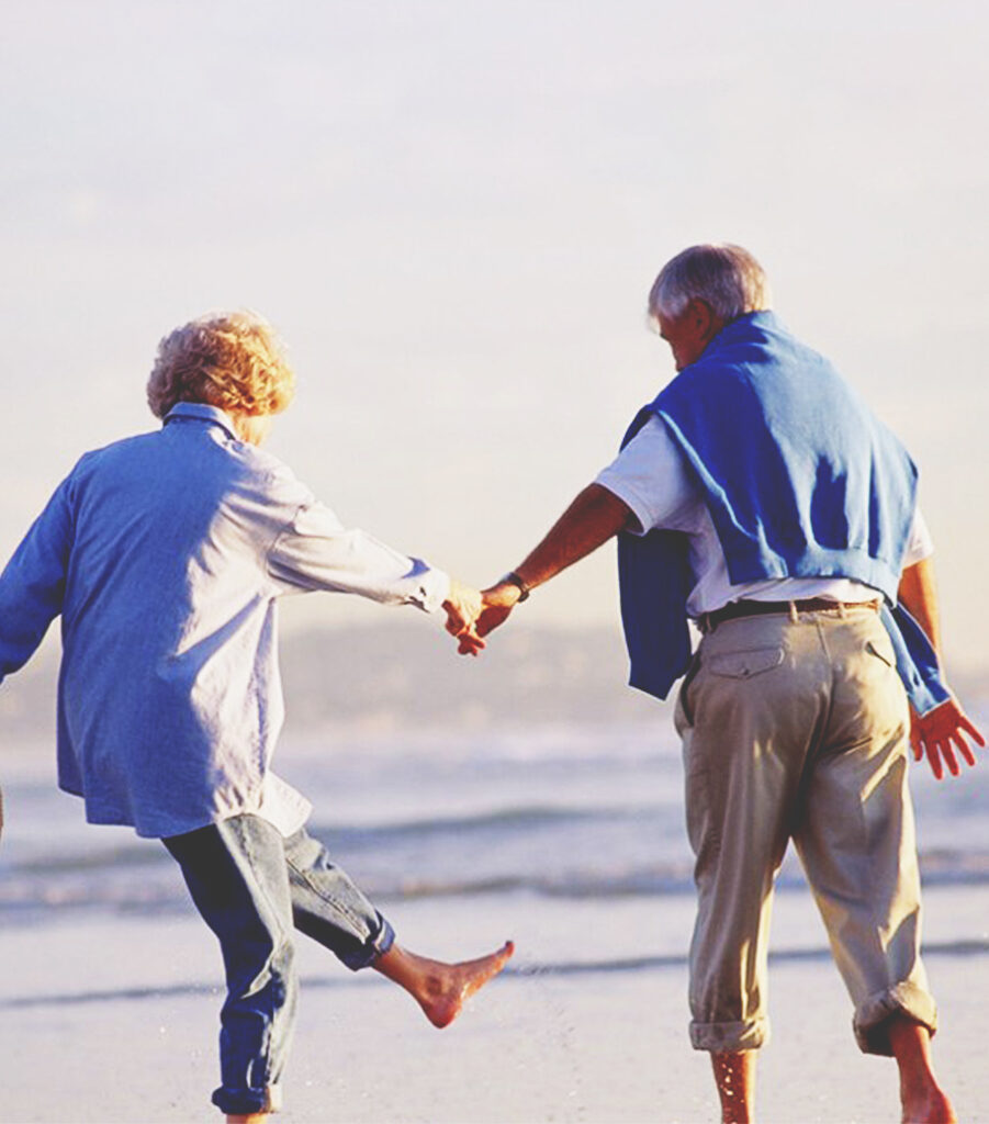 An elderly couple stroll on the beach, holding hands and having a good time together