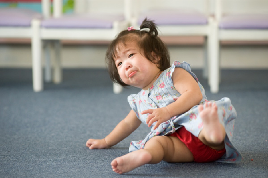 A baby girl in a dress loses her balance while sitting on the floor