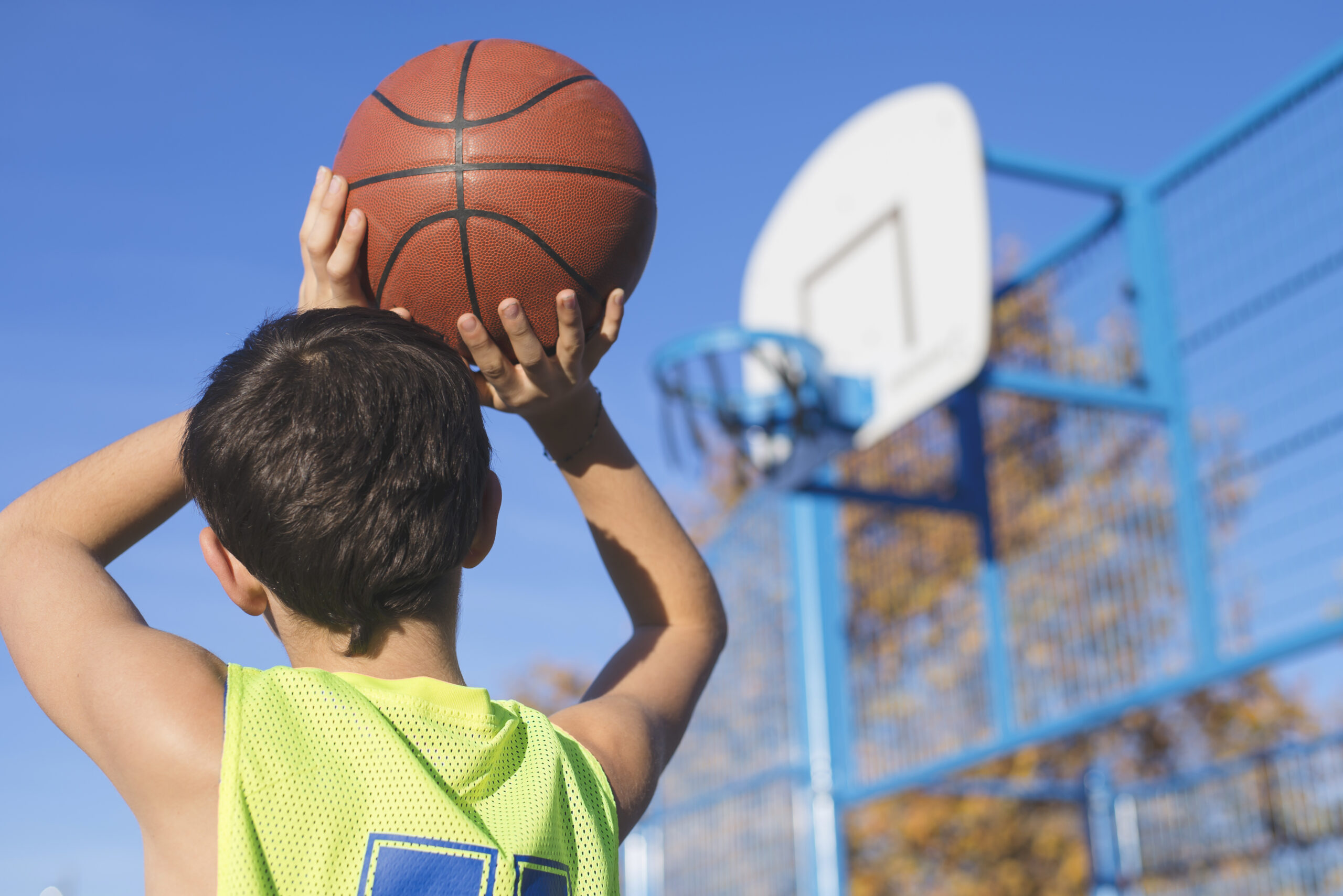 a young boy in green jersey shooting a basket ball into a hoop