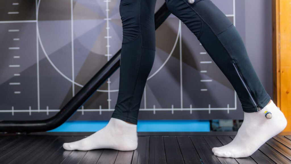 A close-up of a person's legs during a Biomechanical Gait Analysis, showcasing motion tracking technology on a treadmill.