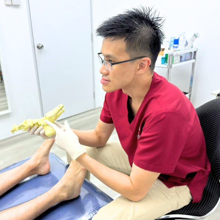 A podiatrist in red scrubs pointing at the heel holding to a human foot skeleton model