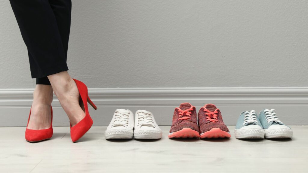 Person wearing red high heels standing next to various casual sneakers, illustrating footwear choices for different occasions.