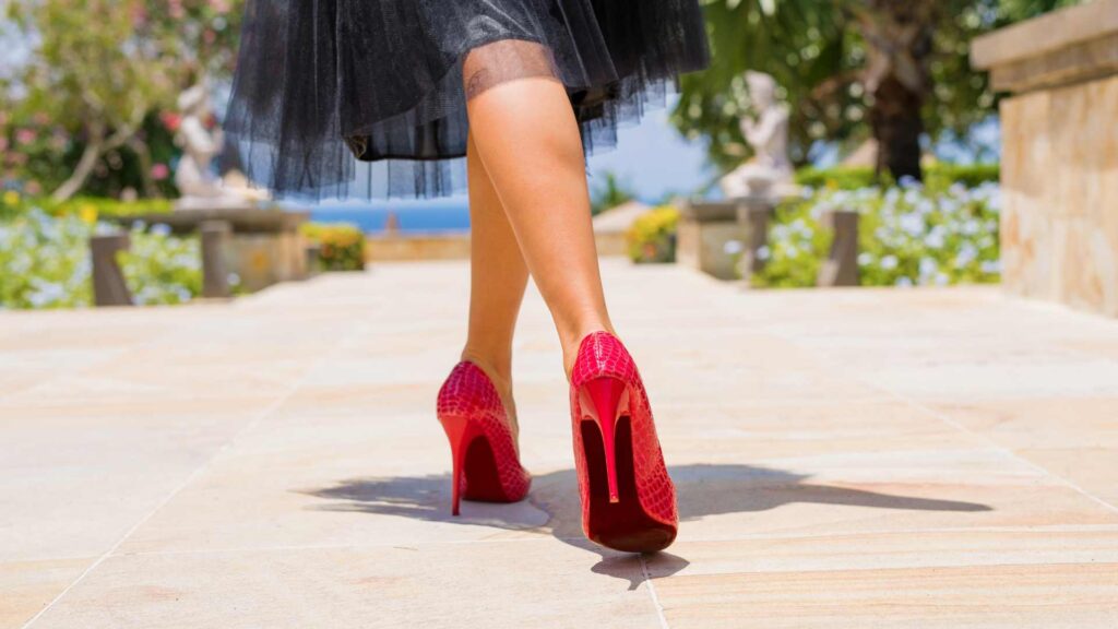 Close-up of a woman walking in stylish red high heels outdoors on a sunny day, showcasing footwear fashion.