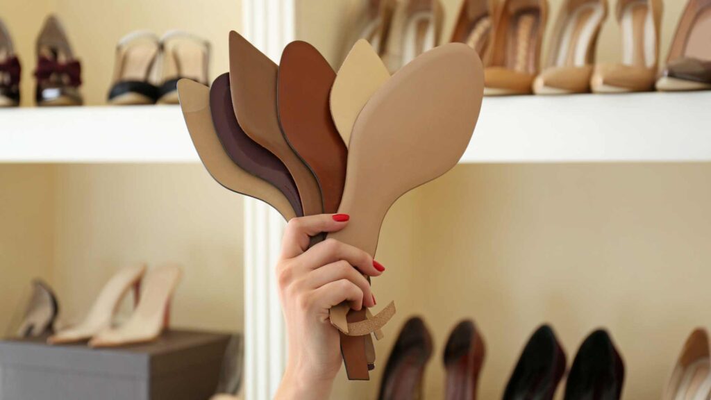 Hand holding a selection of shoe soles in different shades, emphasising the importance of cushioning and support.