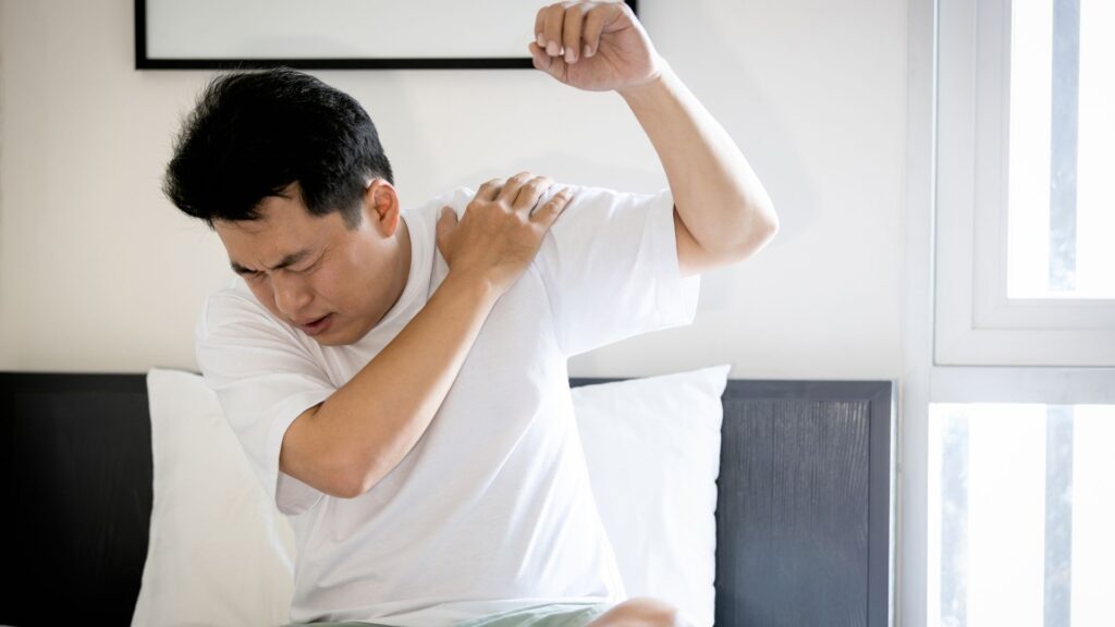 Man in discomfort holding his shoulder, indicating pain and limited mobility, a common symptom of frozen shoulder.