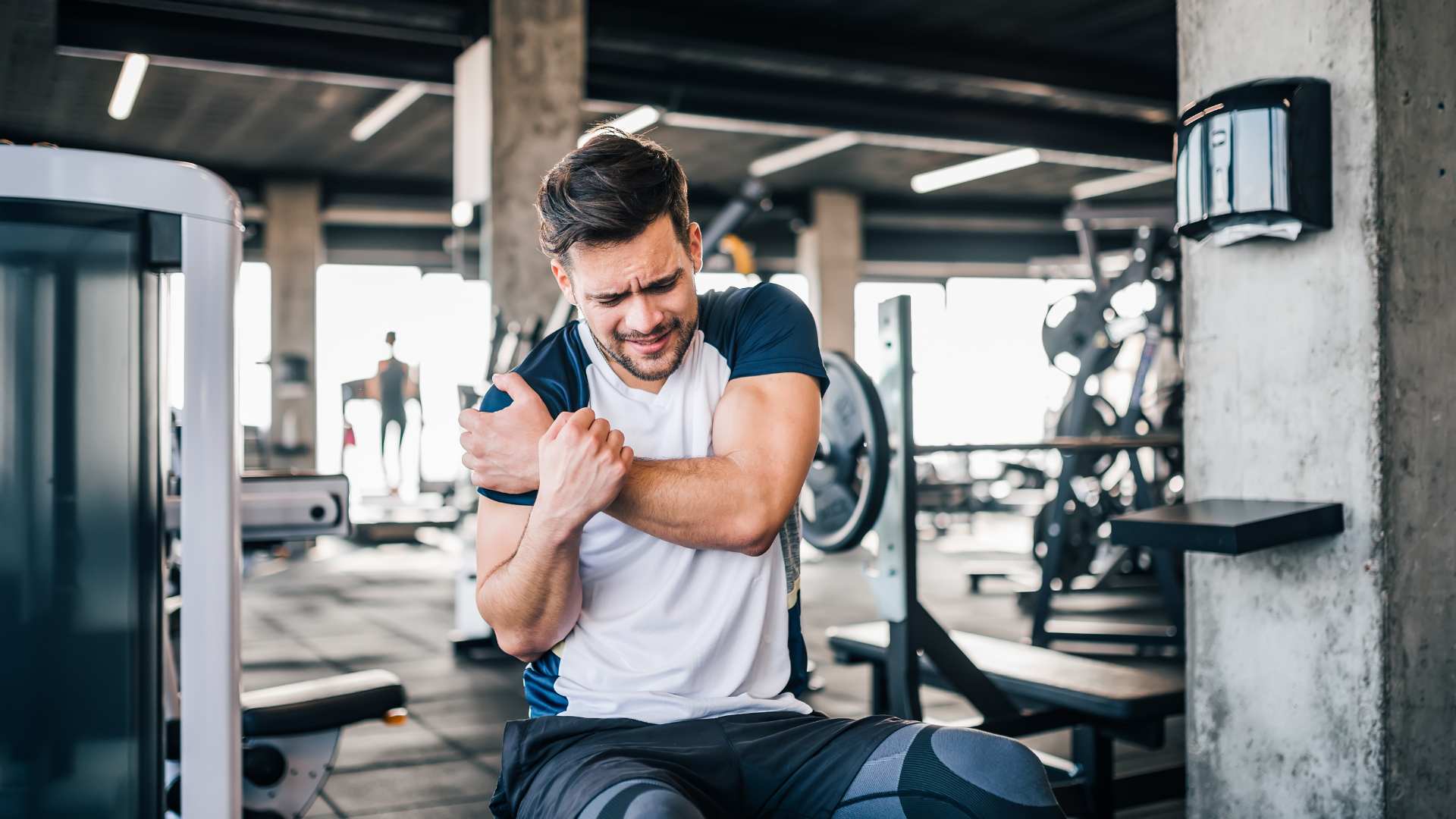 A man in a gym clutching his elbow in pain, showing signs of a sports injury. Proper physiotherapy and treatment can help prevent and recover from workout-related injuries.