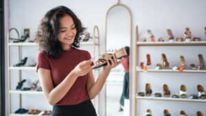 Smiling woman examining supportive footwear in a shoe store, highlighting podiatrist-approved shoe shopping tips.