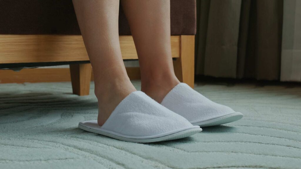 Person wearing white fuzzy slippers on carpeted floor
