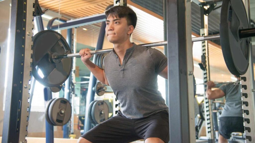 Man performing barbell squats in a gym setting with focused expression