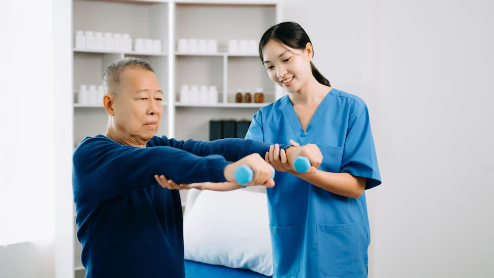 Elderly man doing arm exercises with dumbbells assisted by a smiling physiotherapist
