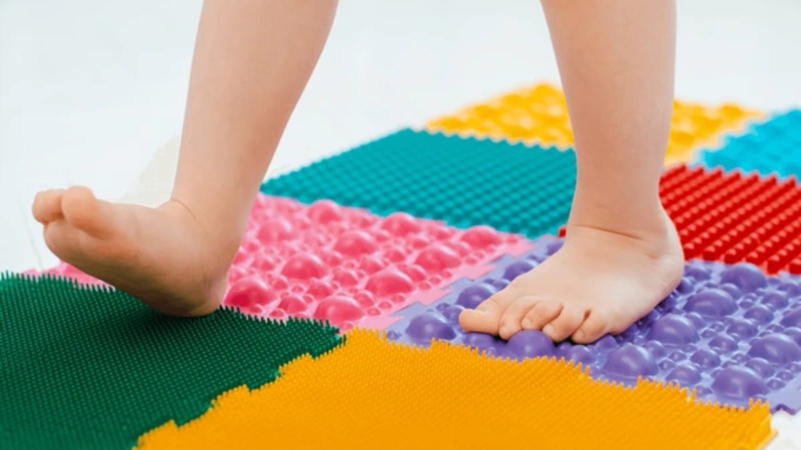 Child walking barefoot on sensory mat, engaging foot muscles and balance.