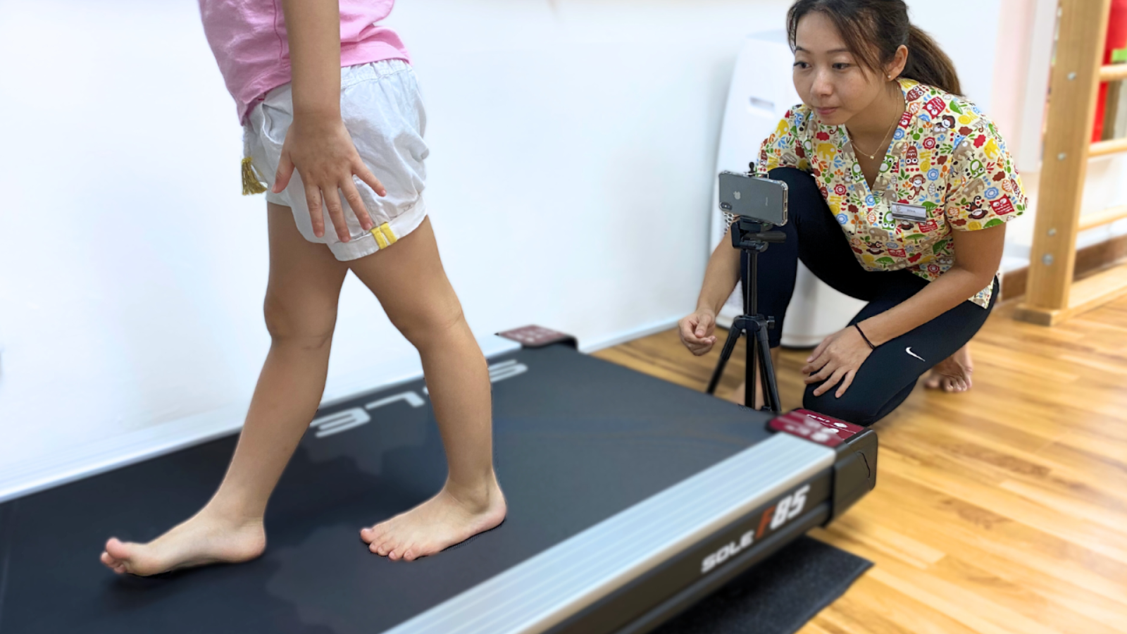 Child walking on treadmill during gait assessment, observed by podiatrist.