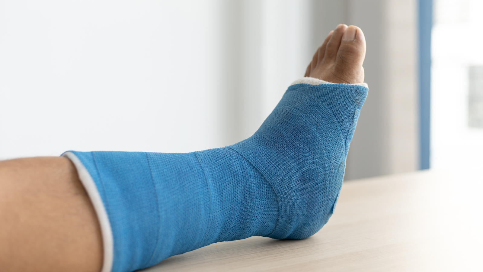 Senior with a foot injury wearing a blue cast, resting foot on table – common foot pain cause in elderly