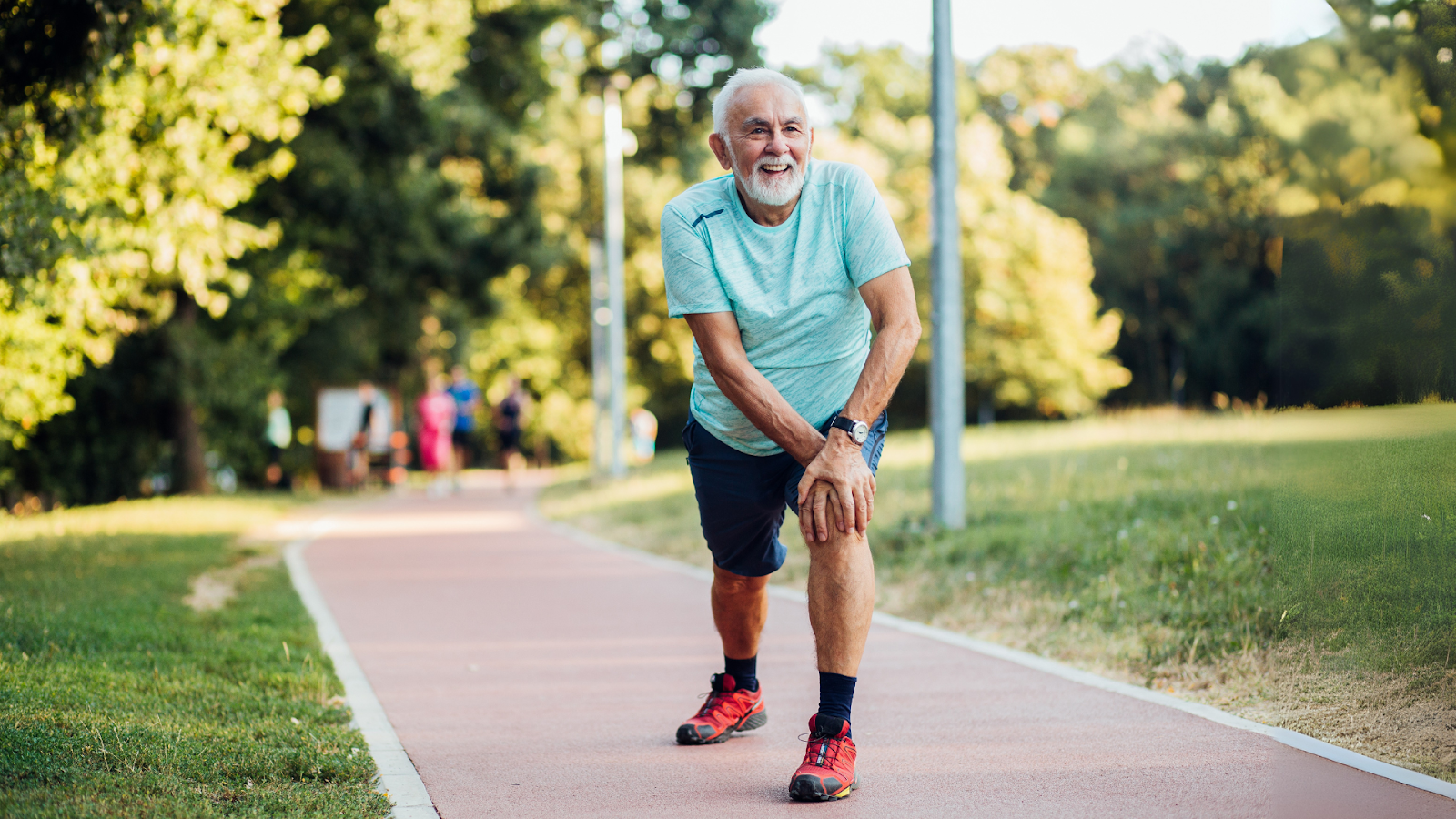 Elderly man holding his knee while walking in a park, indicating joint or foot-related mobility issues