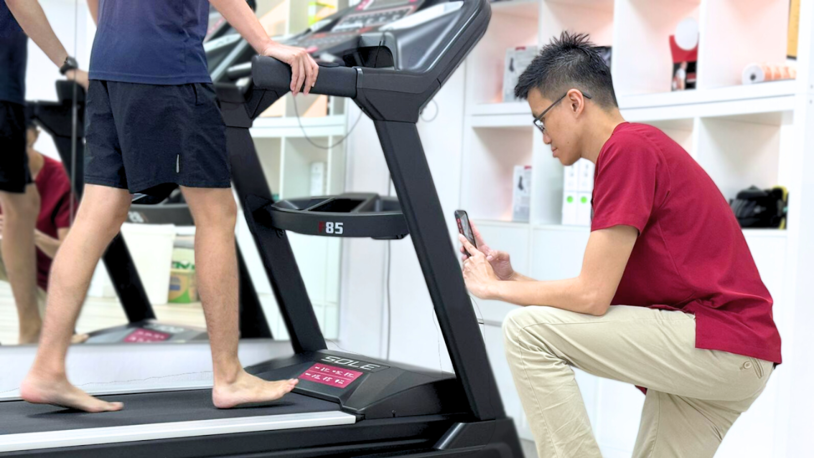 Podiatrist performing gait analysis on a barefoot patient walking on a treadmill to create custom insoles for sports use