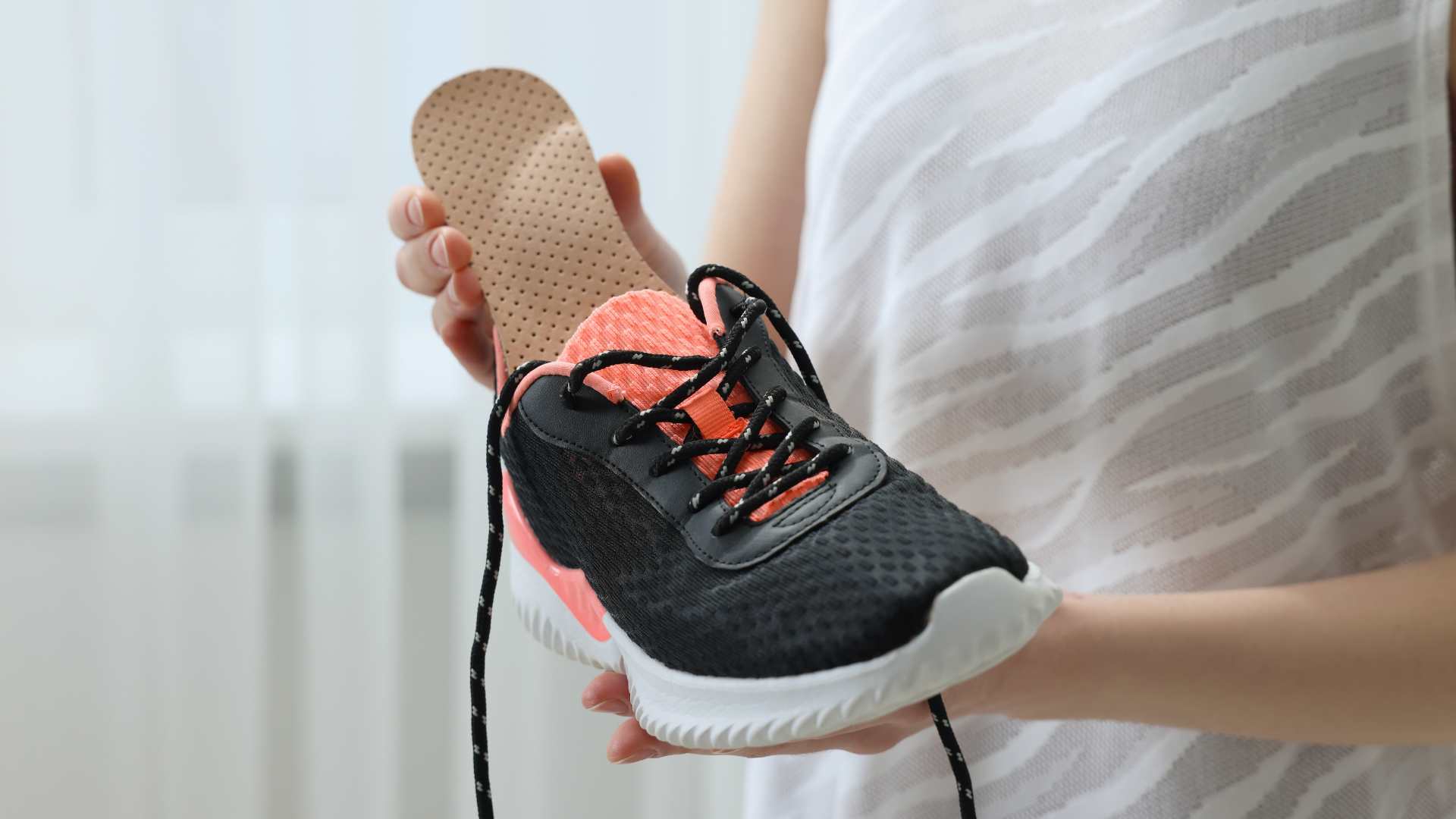 Person inserting custom insole into a black and coral sports shoe for better support