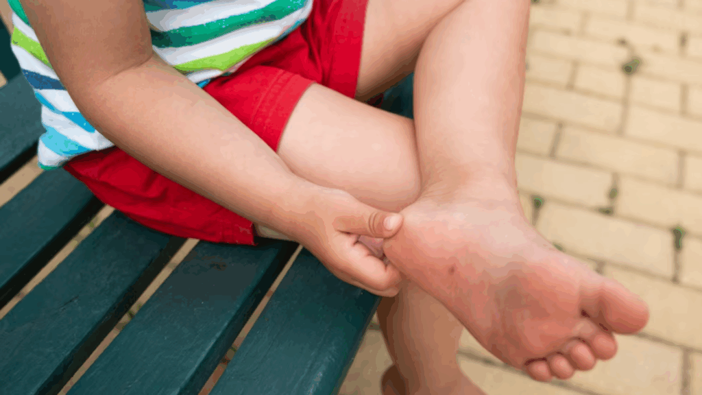 Child sitting on a bench holding their heel due to foot pain – a common concern in podiatry for active kids.