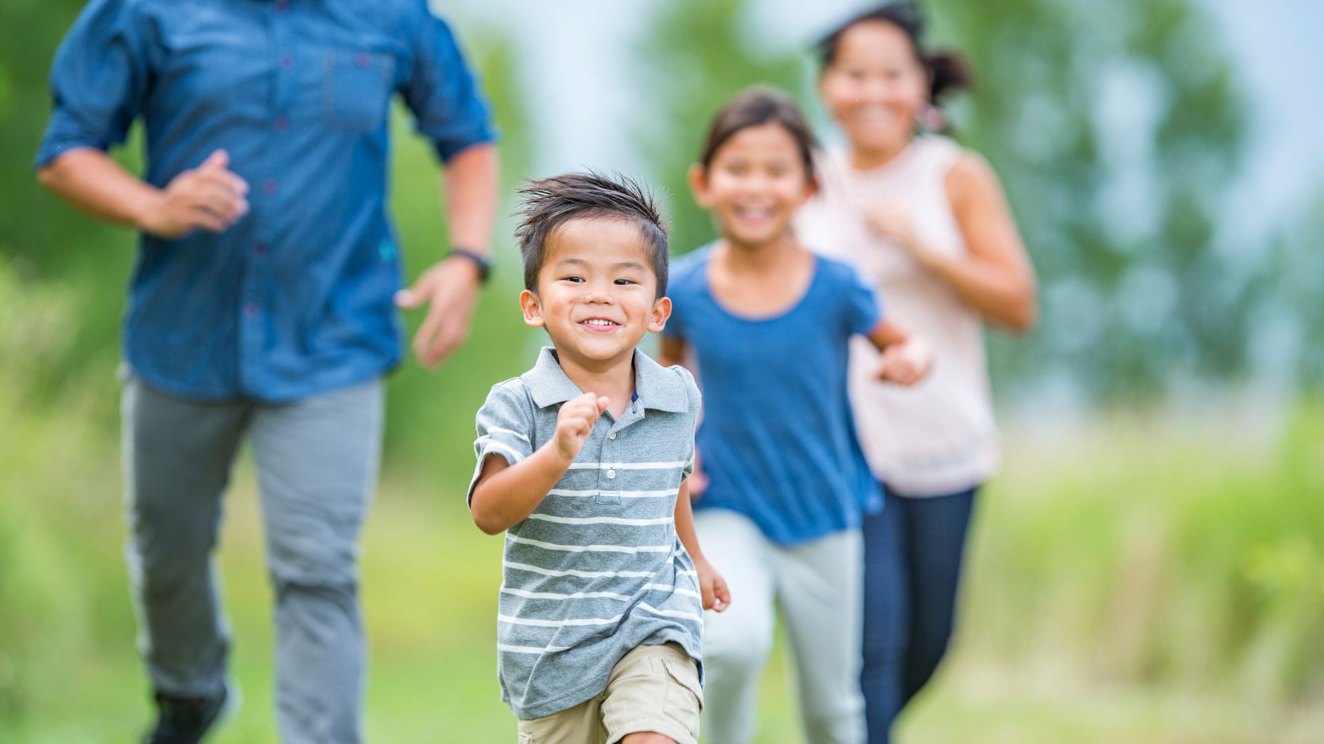 Smiling child running in a park with family in the background, demonstrating healthy gait and joyful movement.
