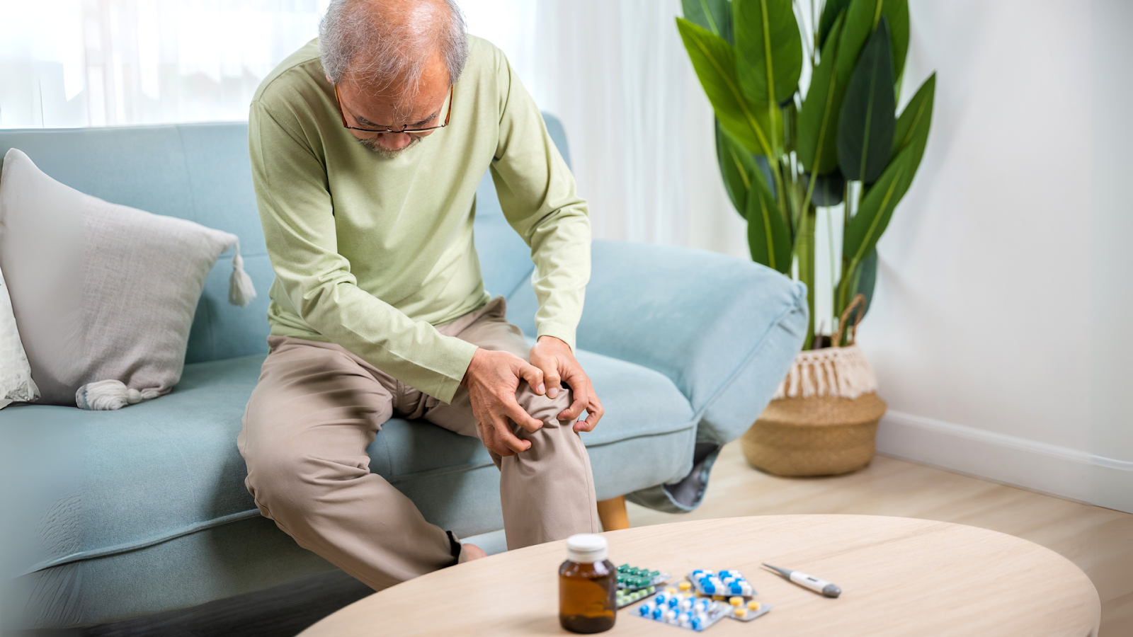 Older man wincing in knee pain at home, representing symptoms of untreated arthritis.