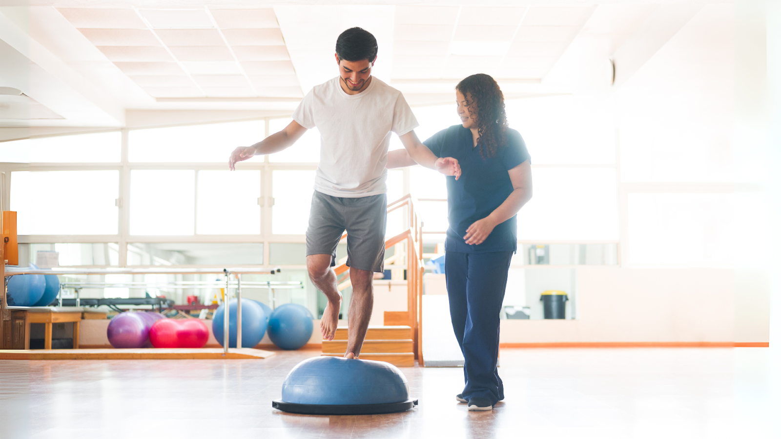  Young adult balancing on a BOSU ball under supervision during post-operative physiotherapy in Singapore