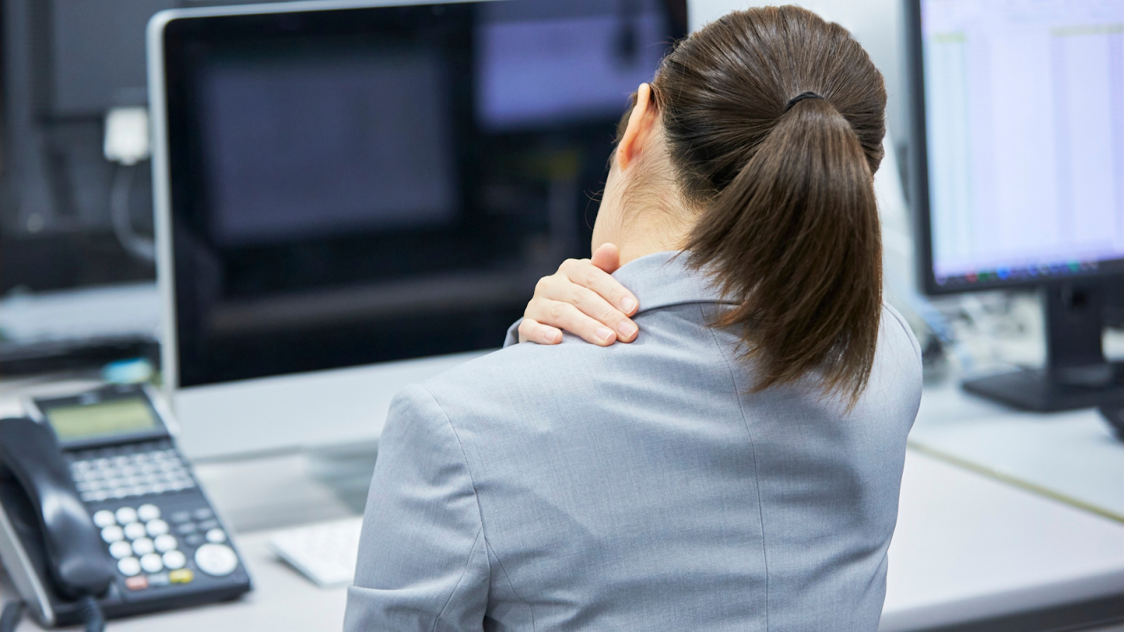 Office worker experiencing neck pain while working at a desk in Singapore