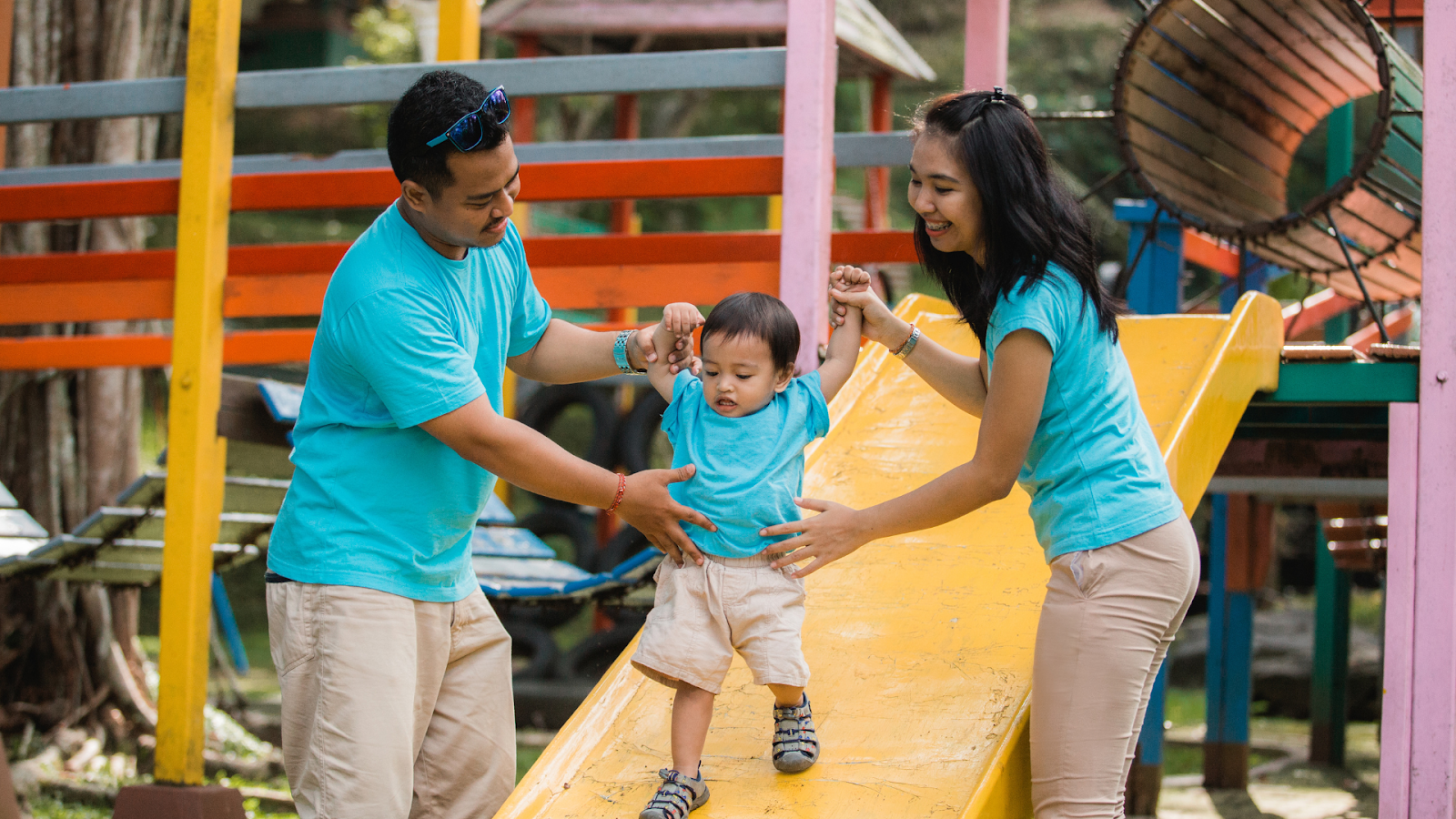  Parents helping toddler on playground slide, supporting safe movement and balance.