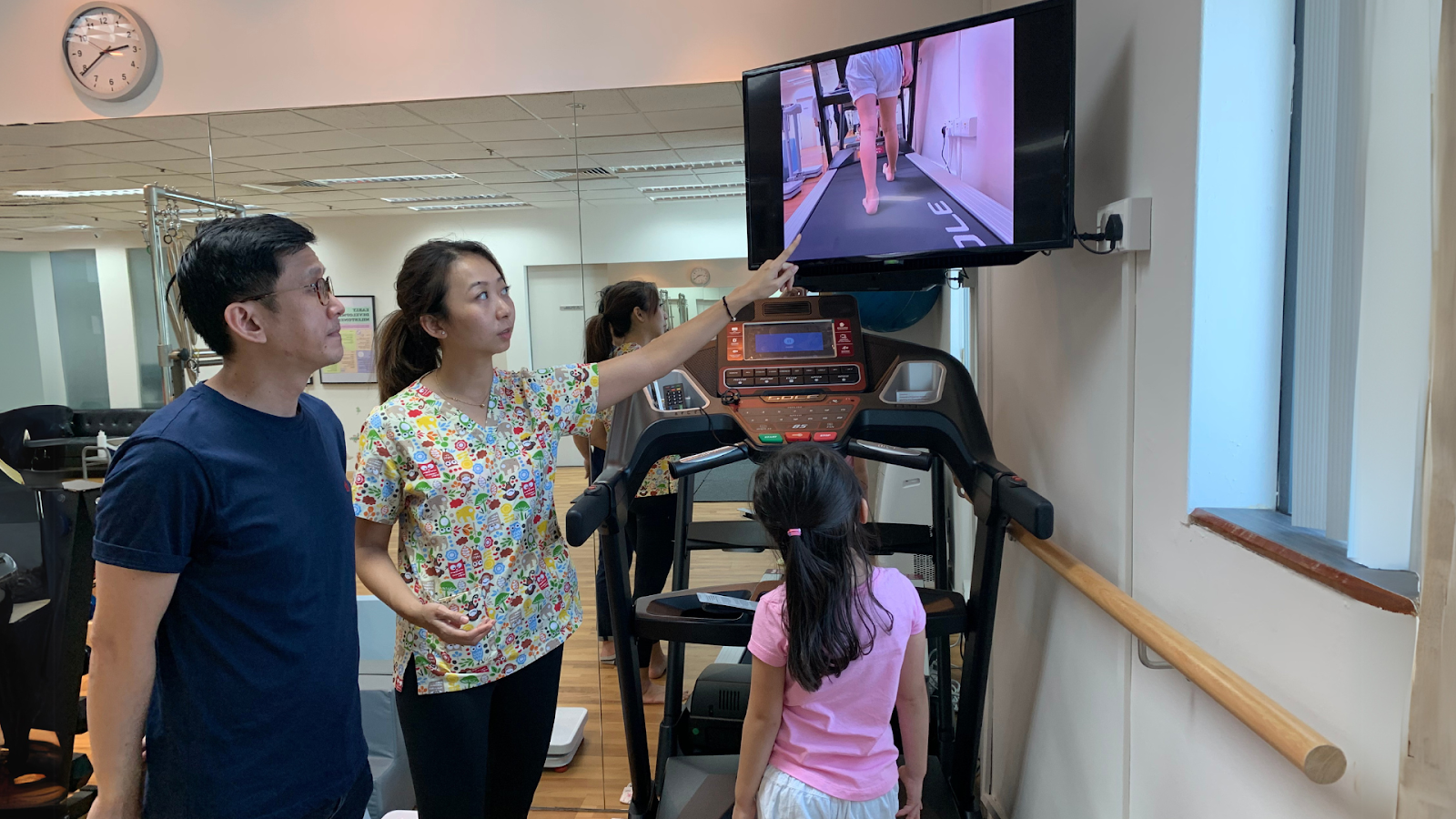 Podiatrist explaining gait patterns to a parent and child during a toe walking assessment session in Singapore.
