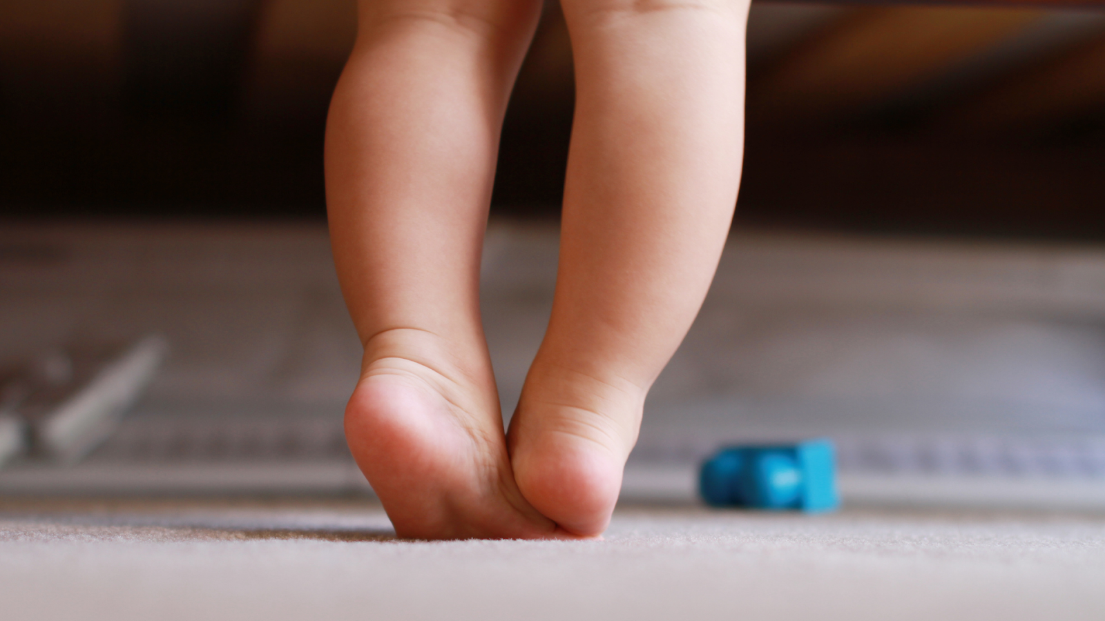 Toddler standing on tiptoes on a carpet, an early sign of toe walking in children often seen during development in Singapore.