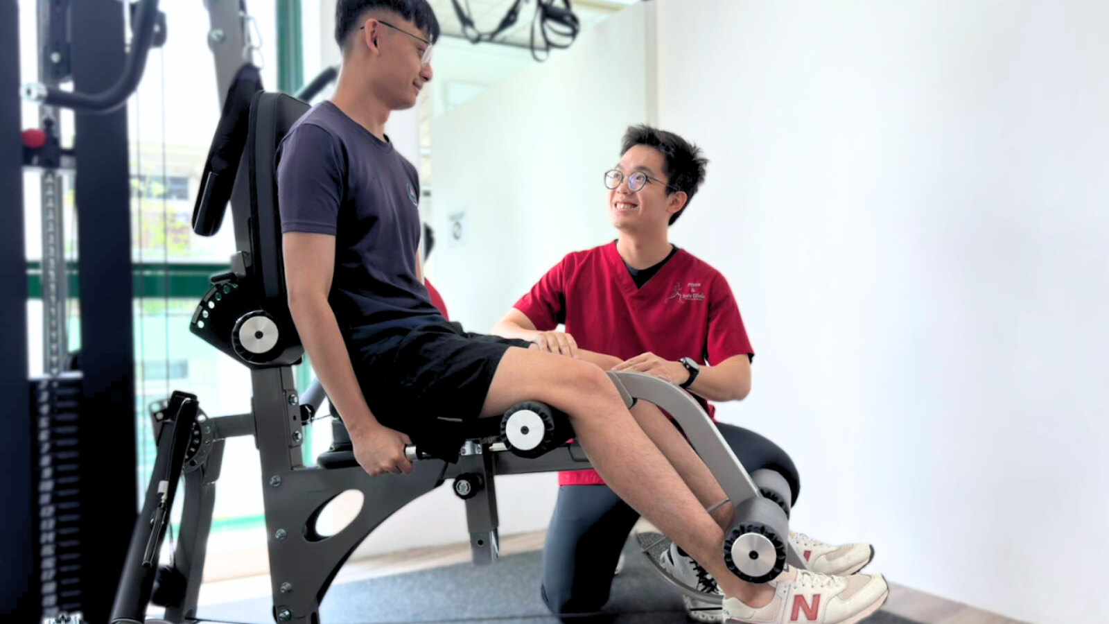 Physiotherapist guiding patient through leg extension exercise on rehab machine for muscle strain recovery.