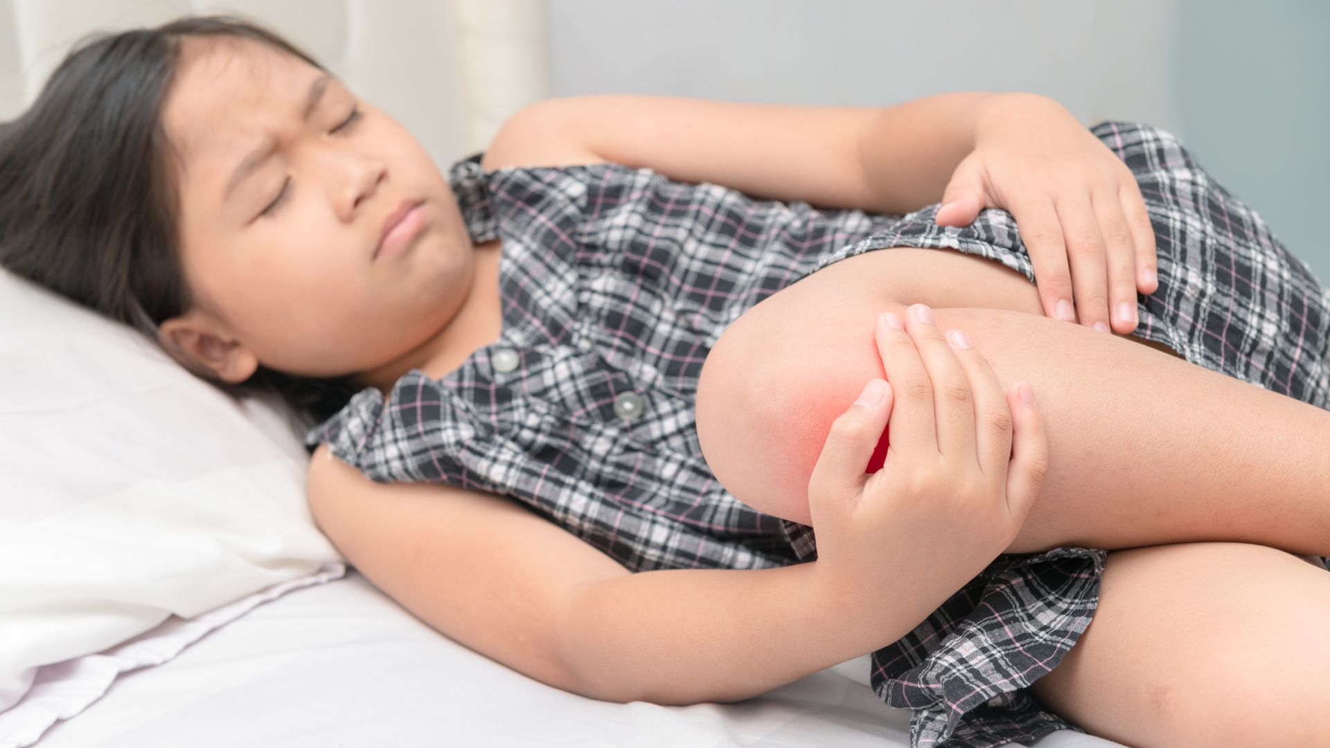 oung girl lying on bed holding her swollen knee in pain, a common sign of Osgood-Schlatter’s Disease.