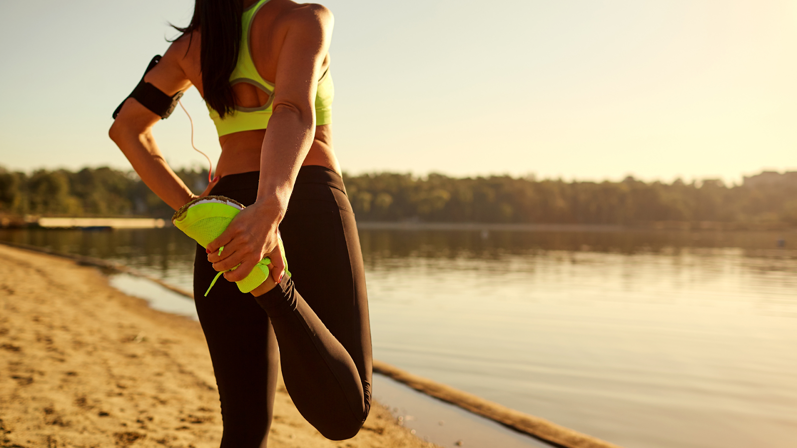 Woman stretching quadriceps to prevent patellofemoral pain syndrome near the lake