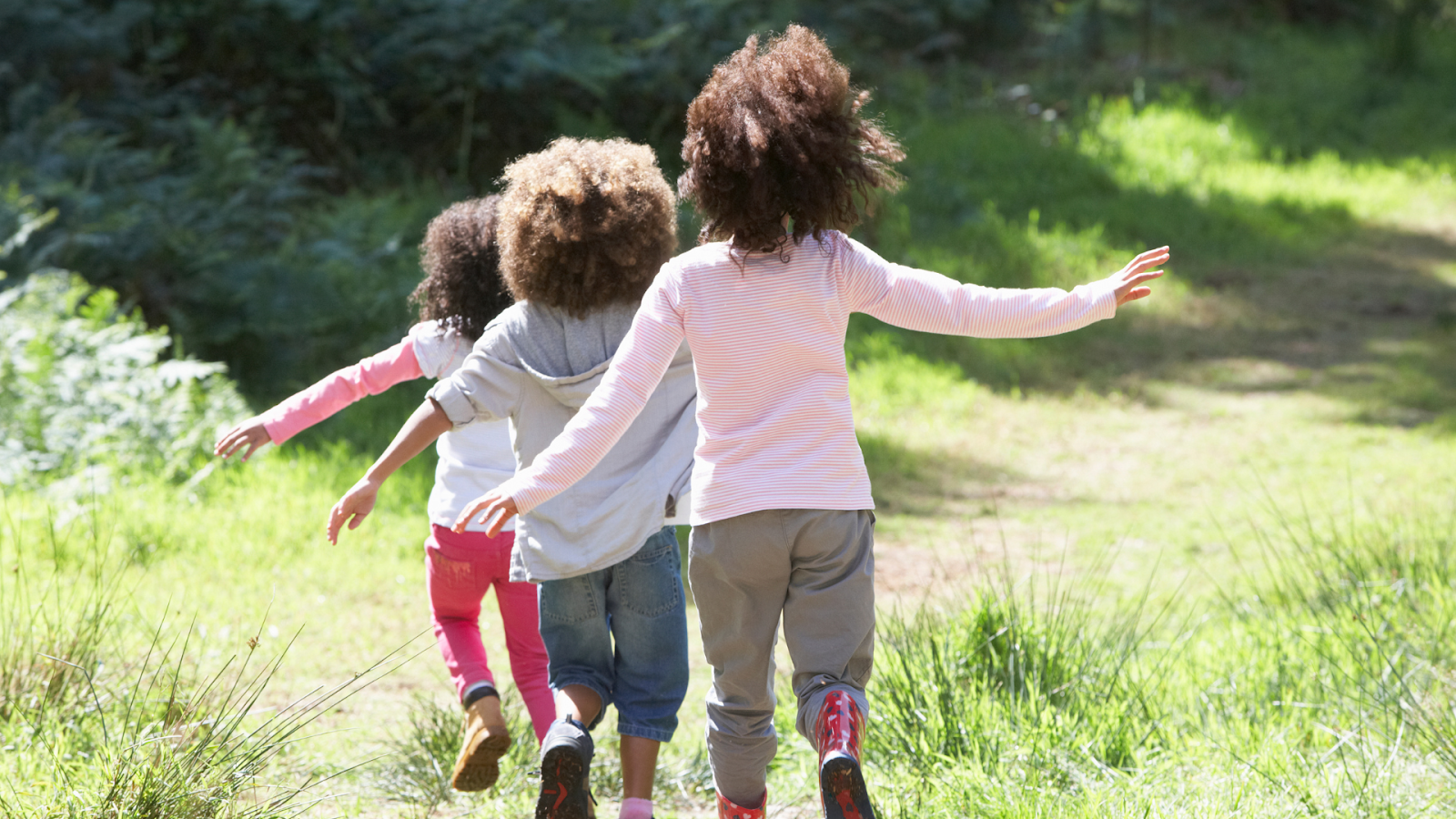 Children joyfully running outdoors on a grassy trail, representing active, healthy play.